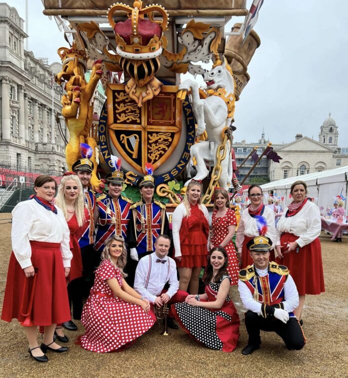 A group of people dressed for a pageant pose in front of a carnival float