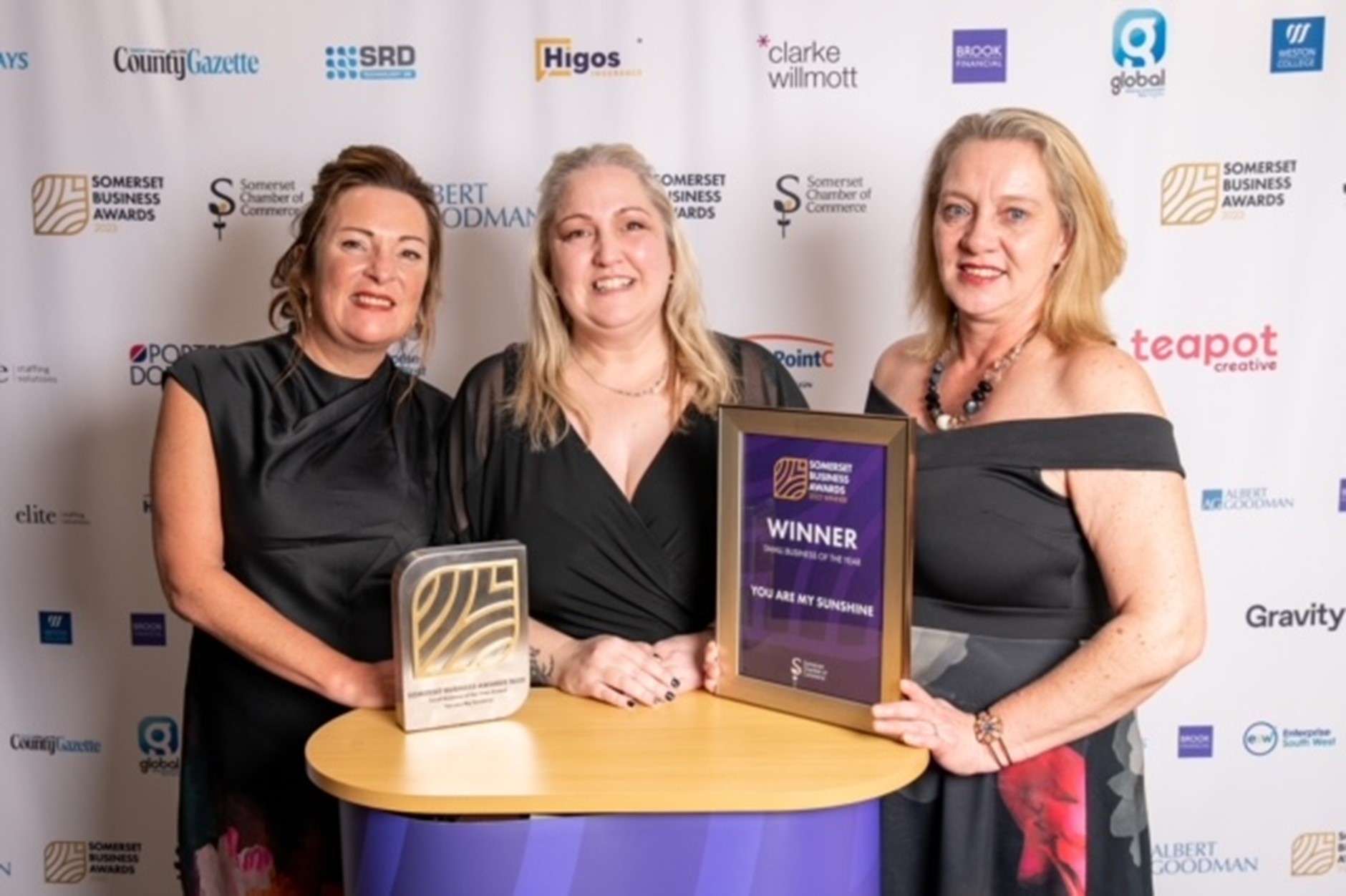 Three women around a podium with awards for Small Business of the Year